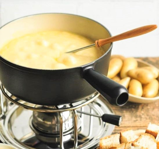 a frying pot on stove filled with Fondue cheese with a basket full potatoes on the table