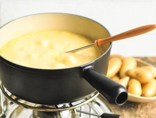 a frying pot on stove filled with Fondue cheese with a basket full potatoes on the table