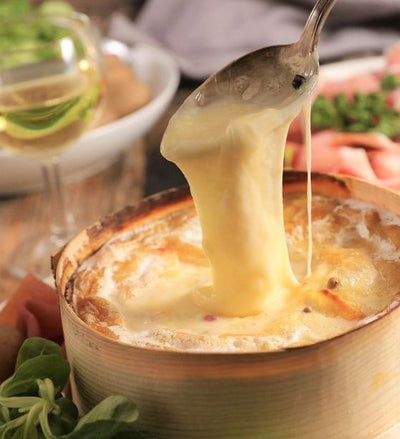 a spoon is dipped into a tin containing Mont d'Or cheese
